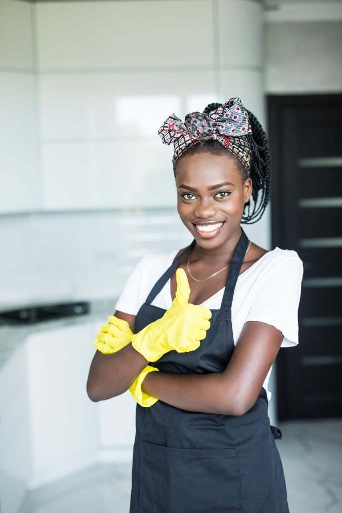 household, cleaning and people concept - happy woman or housewife in rubber gloves wiping table with microfiber cloth at home kitchen and showing thumbs up